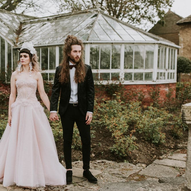 Bride in a pink strapless wedding dress and white 3D flower headband holding hands with her groom in a black tuxedo at Hooton Pagnell wedding venue 