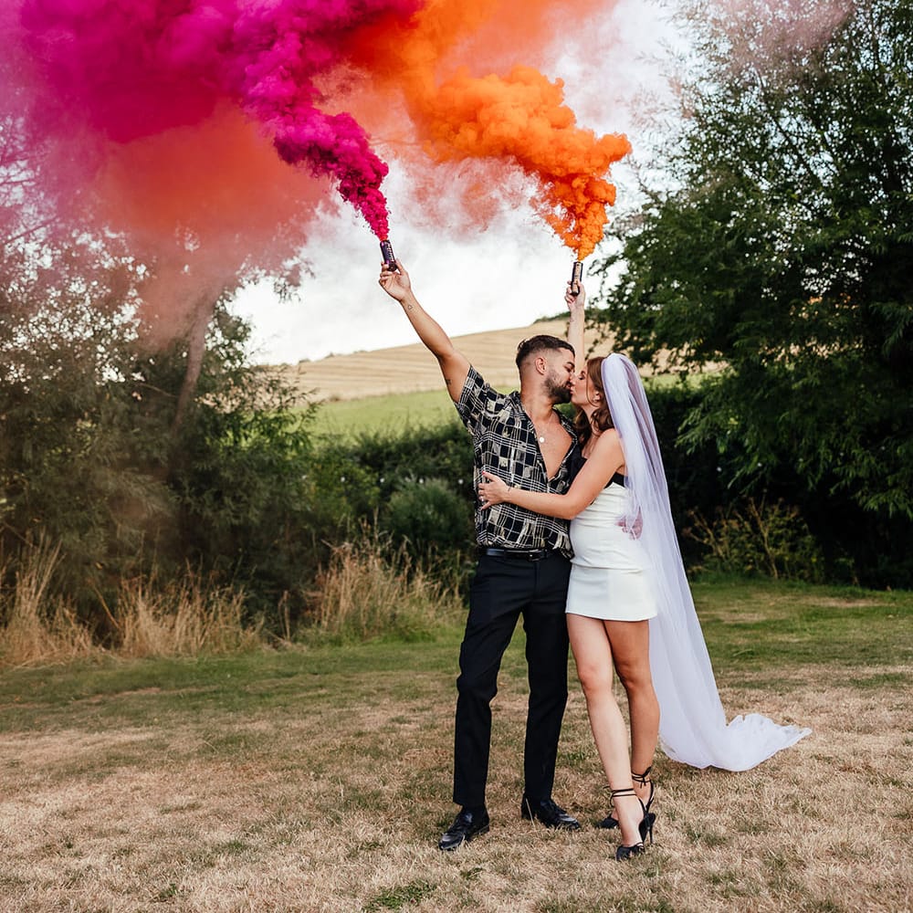 Bride & groom hold pink and orange smoke bombs for outdoor couples portraits