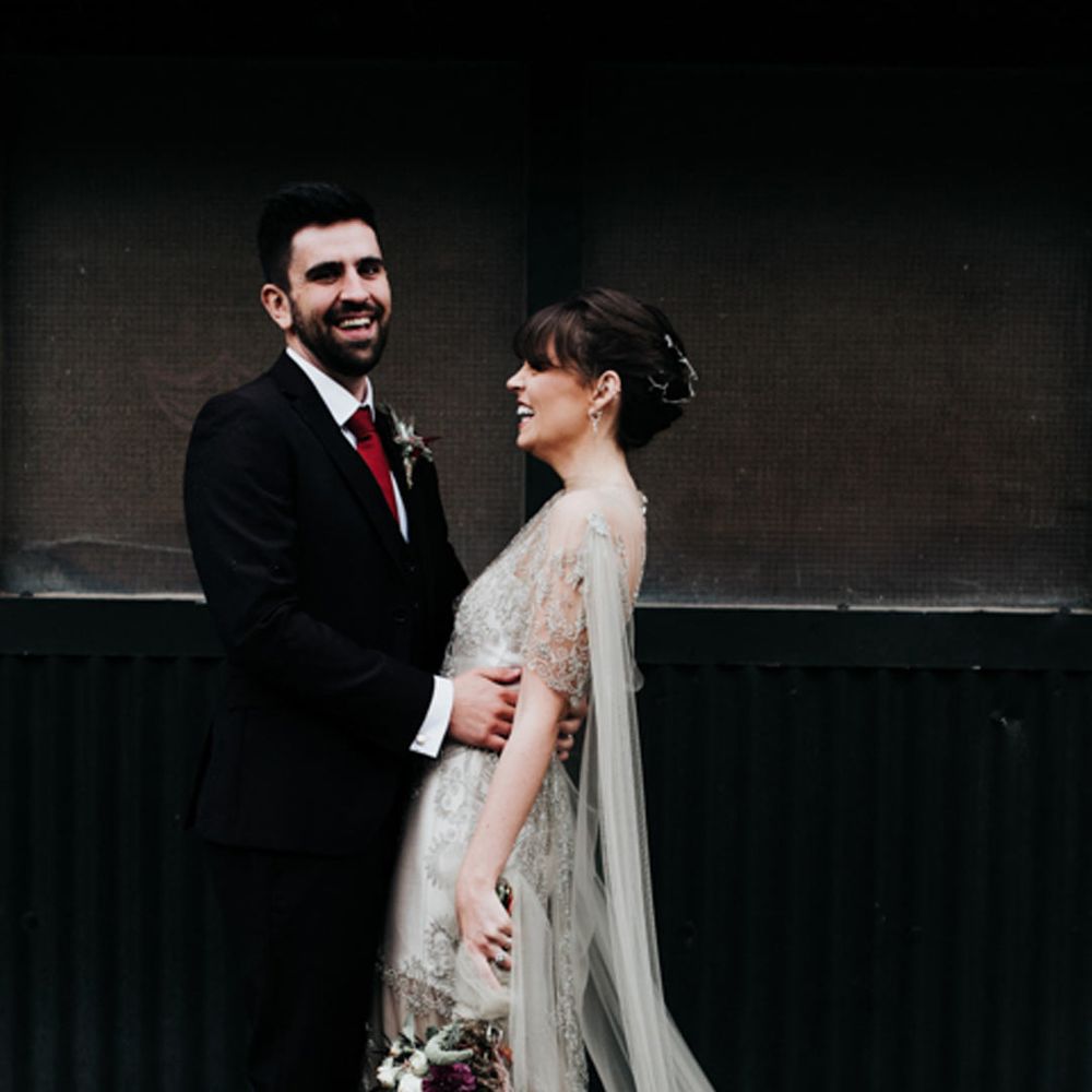 Bride in homemade sage tinted quarter length sleeve wedding dress with homemade bouquet and peacock feathers and groom in dark suit with red tie