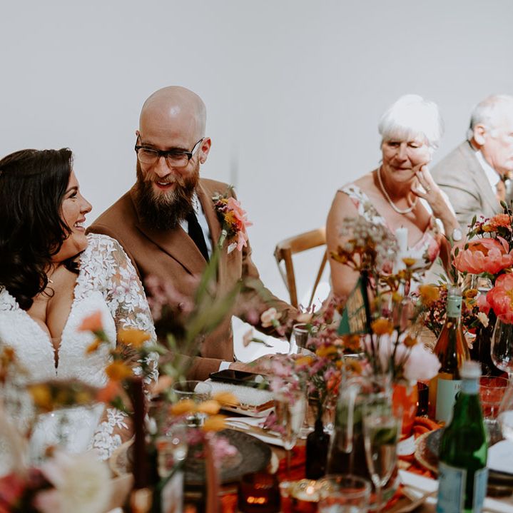 Bride & groom sit at wooden banquet tables during wedding reception in photo studio 