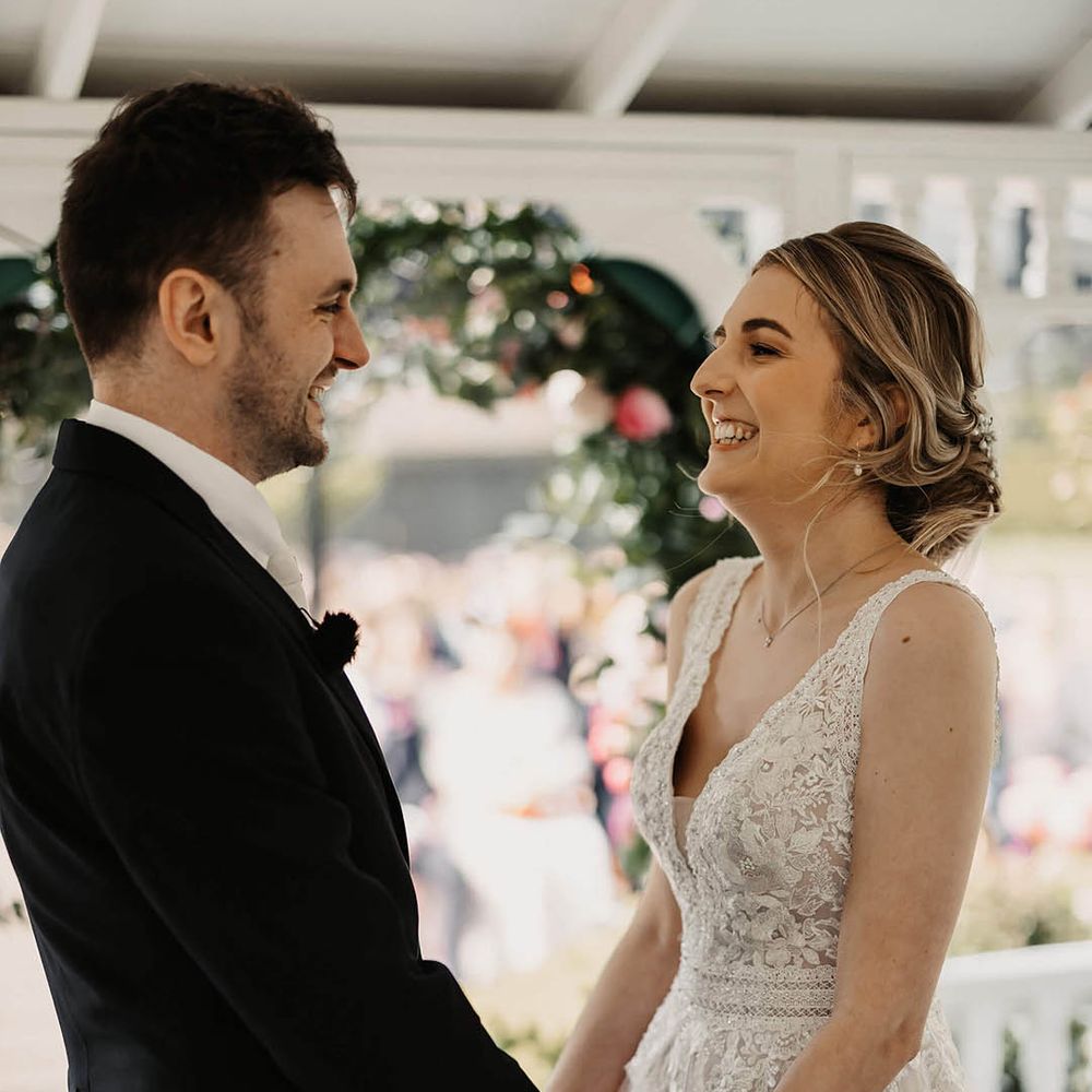 Bride in a lace wedding dress and groom in black three piece suit holding hands for their outdoor wedding ceremony 