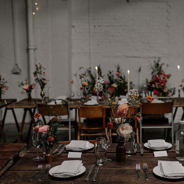 Neutral minimalist Hackney Studios wedding tablescape with tall tapered white dinner candles and pops of colour in floral and foliage decorations