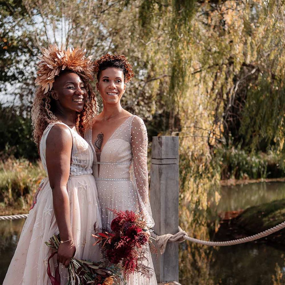 Bride in sleeveless floaty peach gown and gold leaf crown and crystal embellished gown and gold headdress holding autumnal dried flower bouquets standing by the river at Silchester farm 