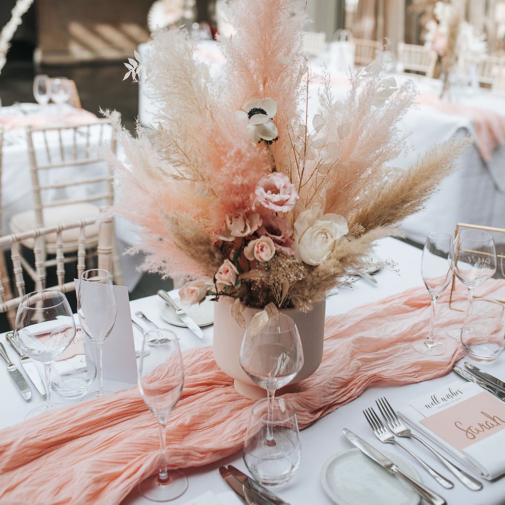 Pink and white pampas grass centrepiece decor with white poppies and roses in a white vase on the table with a pink table runner 