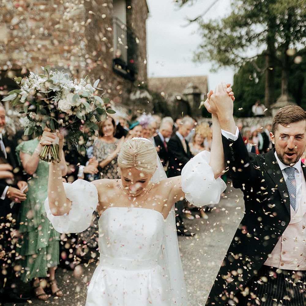 Bride in Jesus Peiro puffed sleeve wedding dress celebrates as she walks through colourful confetti exit with her groom