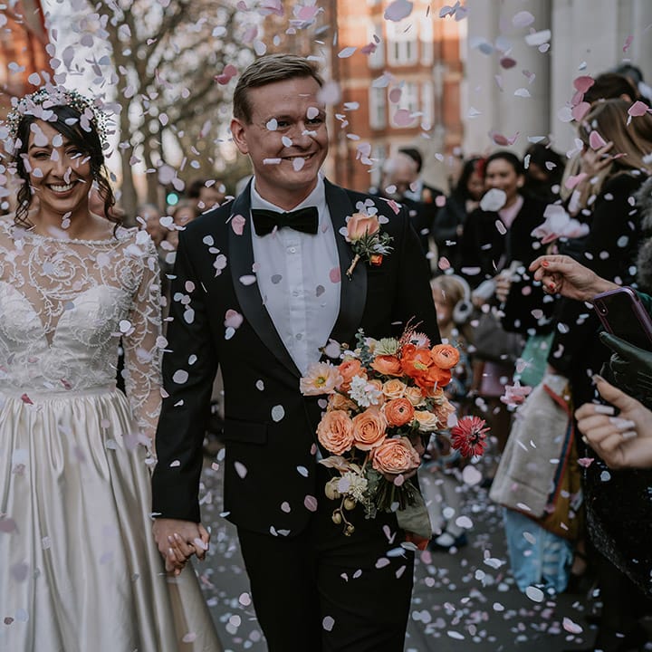 Bride in long sleeve lace wedding dress and groom in classic black tux doing confetti walk at Christmas multicultural London wedding