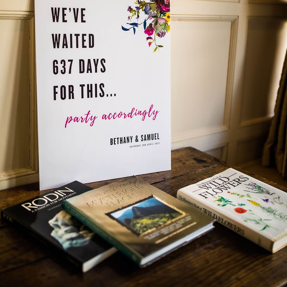 Wedding signage complete with colourful floral illustration on wooden table 