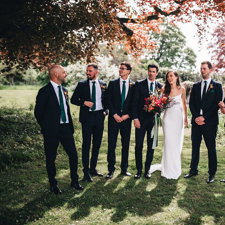 Bride and groom stand laughing with the groomsmen in matching navy suits and green ties for the wedding 