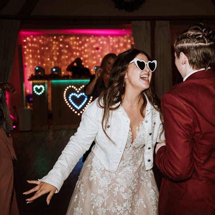 Bride in heart shaped wedding sunglasses dancing at wedding party with bride 