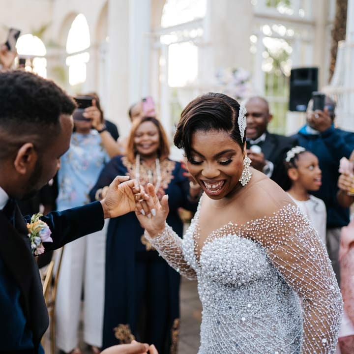 Bride in illusion v neck sheer off shoulder long sleeve pearl embellished wedding gown dancing with groom in velvet midnight blue double breasted groom’s blazer, velvet bowtie and peach garden rose boutonniere at Syon Park vow renewal