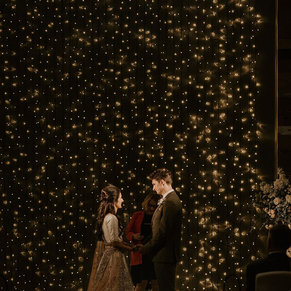 The bride and groom stand together under cosy magical lighting for multicultural ceremony 