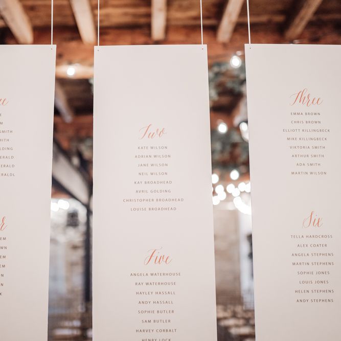 Hanging seating chart with gold font table names 