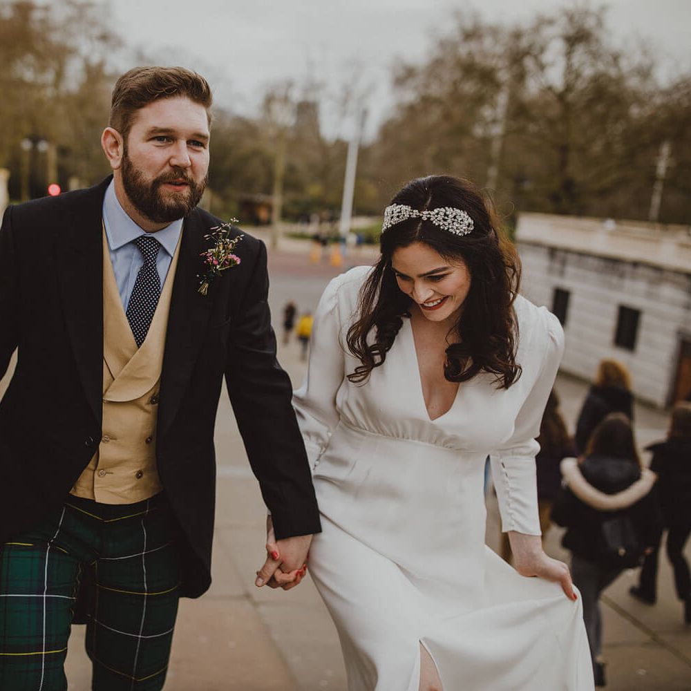 Bride and groom walking up steps outside in London, groom wears three piece suit with tartan trousers, bride wears long sleeve silk wedding gown 