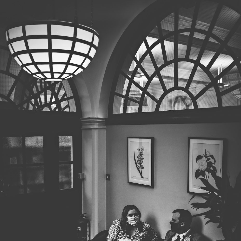 Bride & groom wears masks in black & white image as they sit within Chelsea Old Town Hall