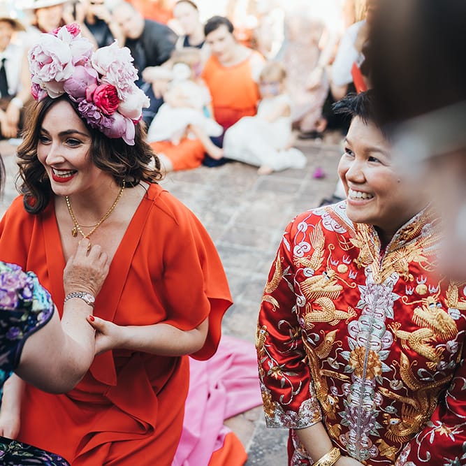 Bride smiles and laughs whilst wearing red dress and pink floral crown outdoors
