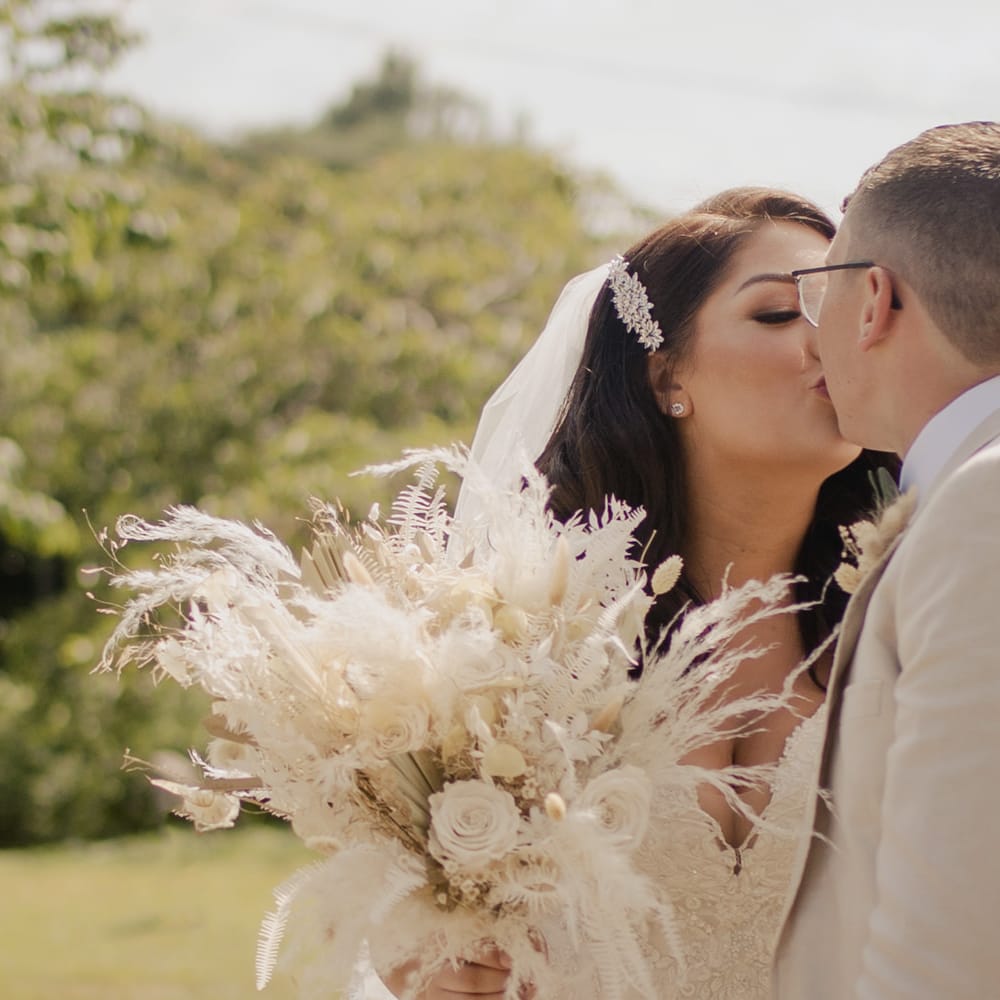 Bride with side swept wedding hairstyle holding a neutral dried flower wedding bouquet whilst kissing her groom 