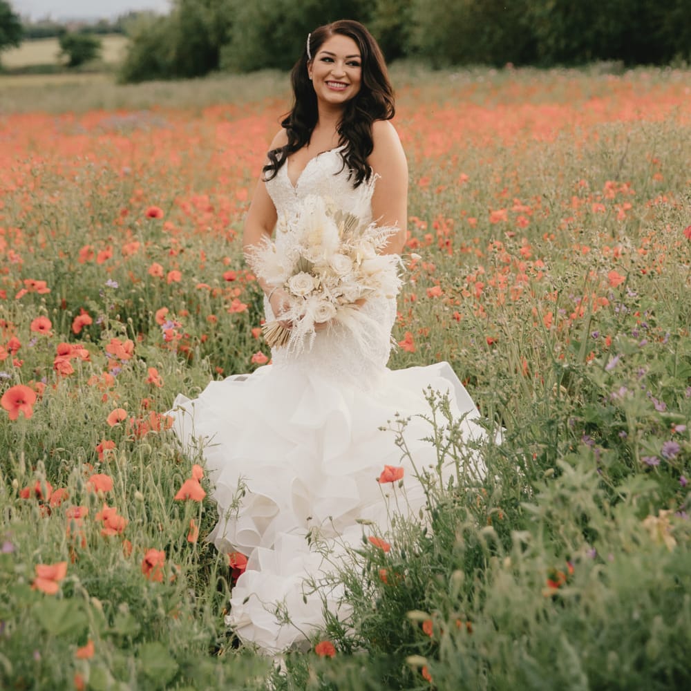 Beautiful bride standing in a poppy field in a Mori Lee fishtail wedding dress holding a neural dried flower wedding bouquet 