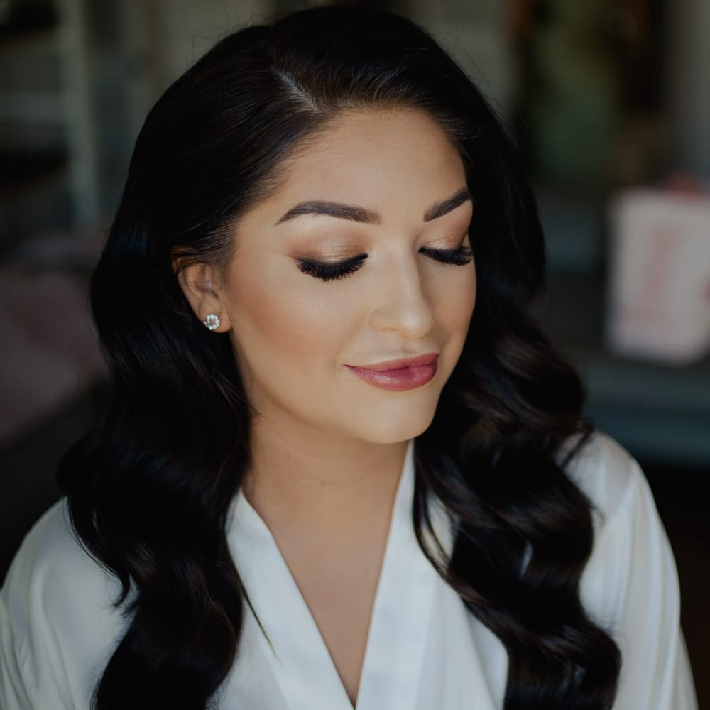 Bride with long wavy side swept hair and flawless bridal makeup with shimmering eyeshadow and deep pink lipstick. 