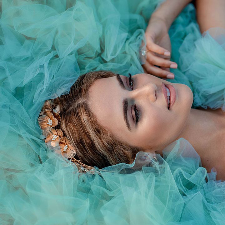 Bride with smokey brown and green eyeshadow and gold headdress laying on top of her mint green layered tulle wedding dress 