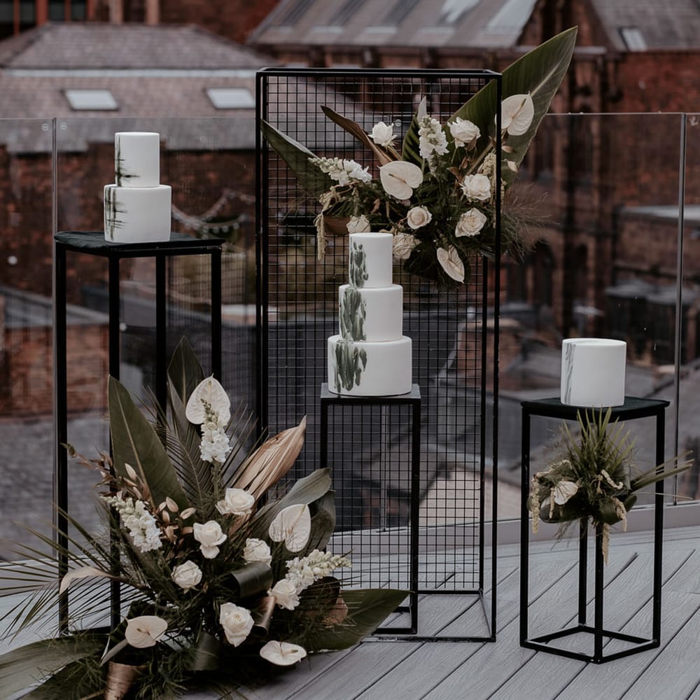 Wedding cake display on the roof terrace at Manchester Hall with white and green iced cakes surrounded by tropical flowers and leaves