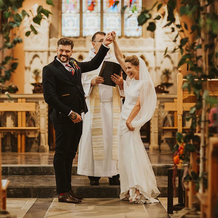 Bride and groom holding hands at the altar of their church wedding ceremony decorated with trees 