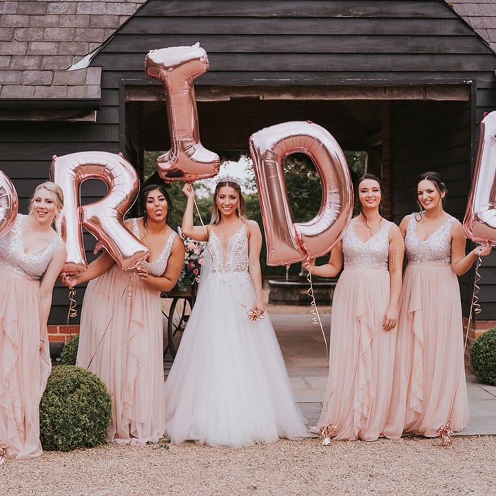 Bride and bridesmaids in stunning pink dresses in front of 'bride' balloons