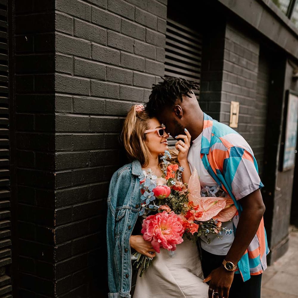 Groom in a patterned shirt embracing his bride in a short wedding dress and denim jacket at their stylish urban elopement 