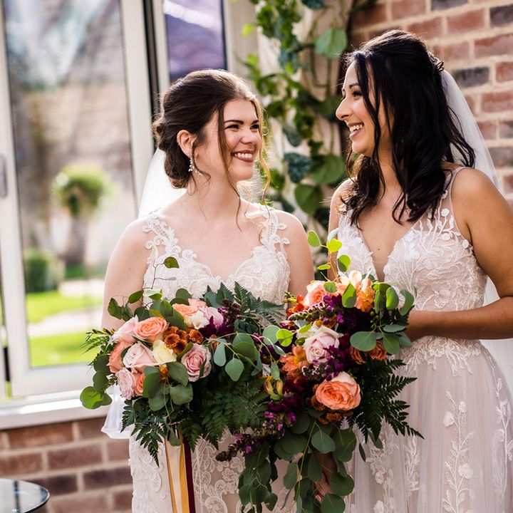 Brides in floral lace dresses with wedding bouquets with purple, orange and pink flowers include roses and fern leaves 