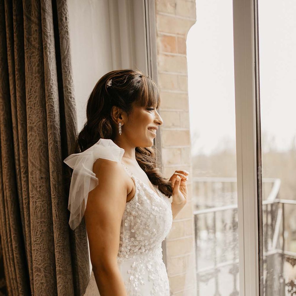 Bride in traditional white wedding dress (before mint green saree) with shoulder detail and long silver earrings