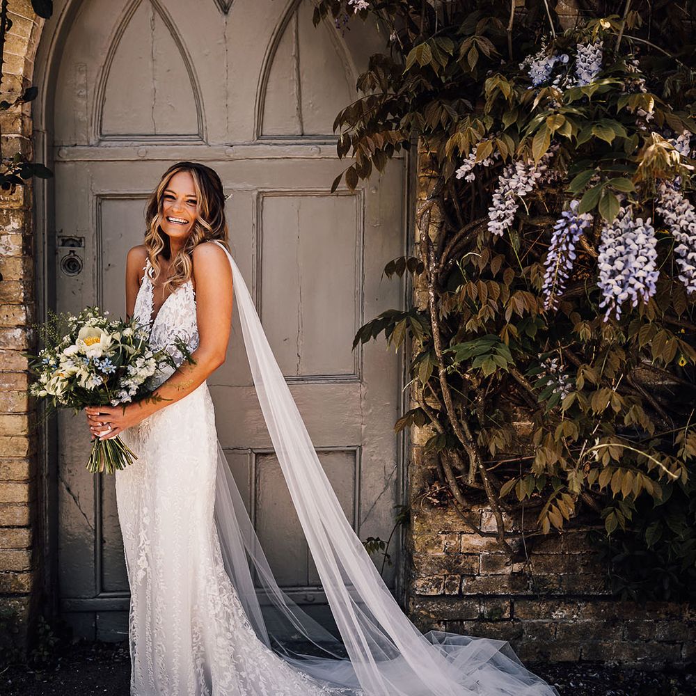 Bride holding yellow and blue bouquet with bride in lace wedding dress with train and detachable tulle wings 