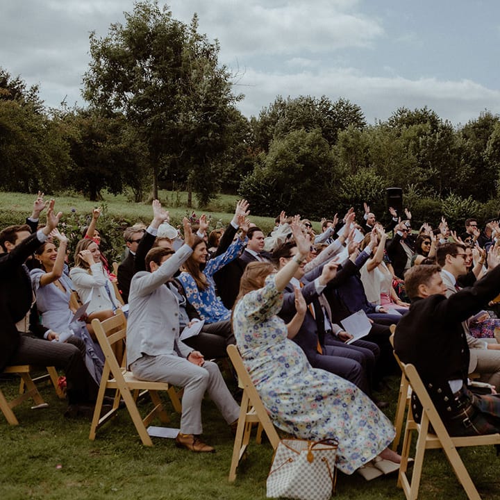 Wedding guests raise their hands as part of the outdoor wedding ceremony at Owlpen Manor 