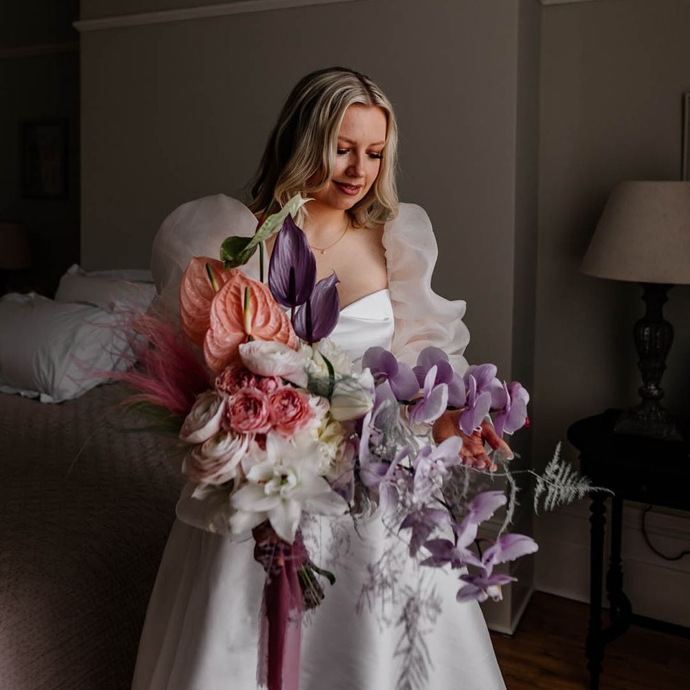 Bride in a JESUS PEIRO wedding dress holding a lilac orchid, pink anthurium and white lily bouquet 