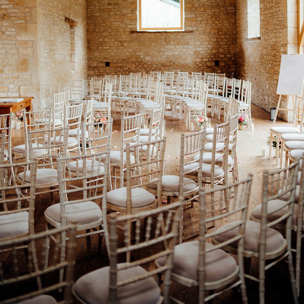 Fairy lights hang above white wicker chairs in rustic room with exposed brick for barn wedding ceremony