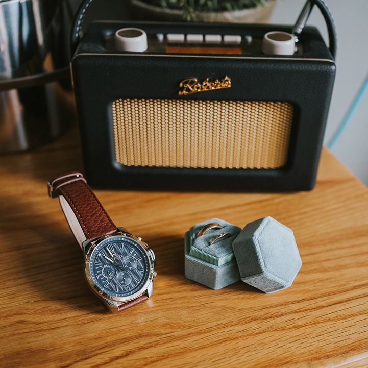 Groom's brown leather watch strap with a blue velvet ring box in front of the black radio 