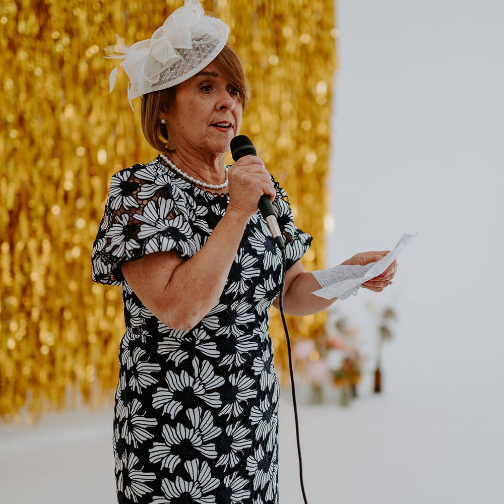Wedding guest gives speech during reception in front of gold streamers wedding decor 