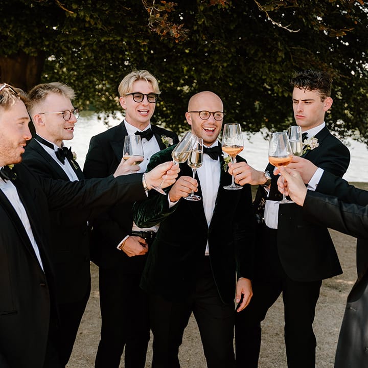 Groom wears black tie surrounded by his groomsmen in matching suits 