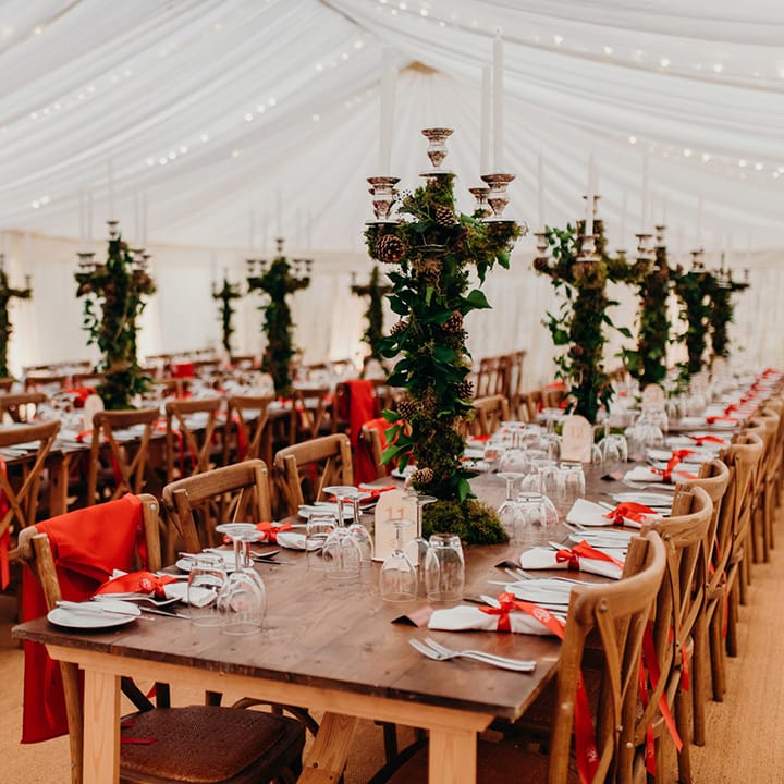 Reception room at Christmas themed wedding with red napkins, chair covers and winter foliage decorated candle holders
