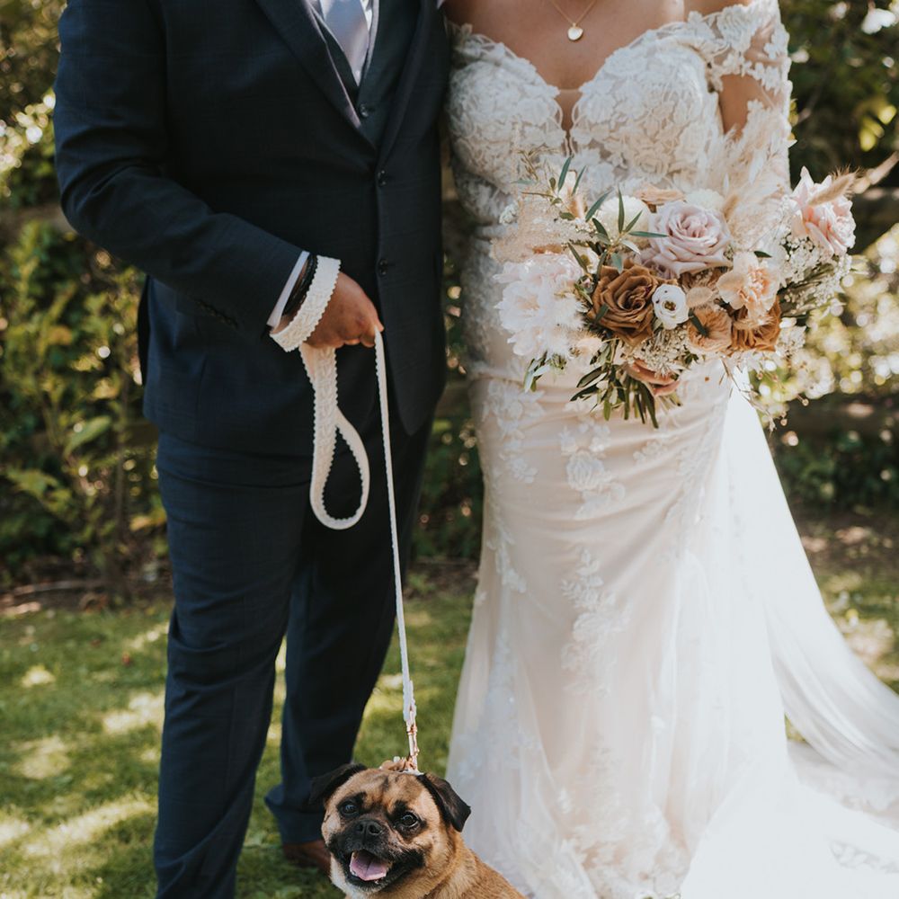 Bride & groom stand outdoors with their pet dog on their wedding day in Devon