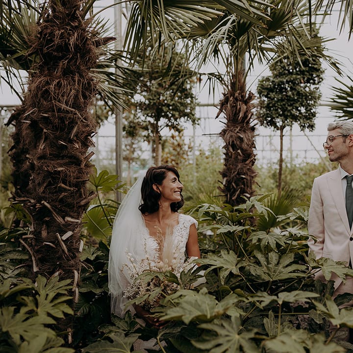 Couple pose and smile surrounded by plants and trees