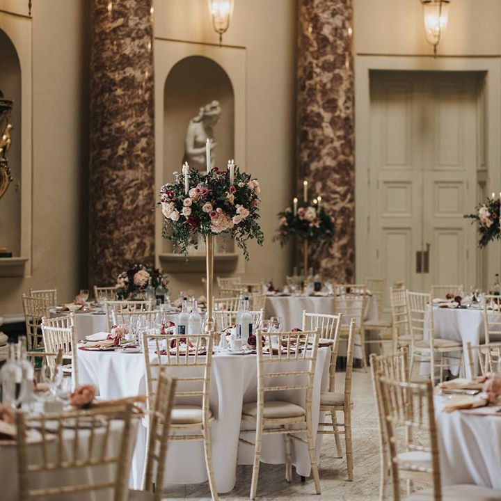 Stowe House wedding reception room with circular tables covered with white tablecloths, tall candelabra centrepieces with pink and red flowers 