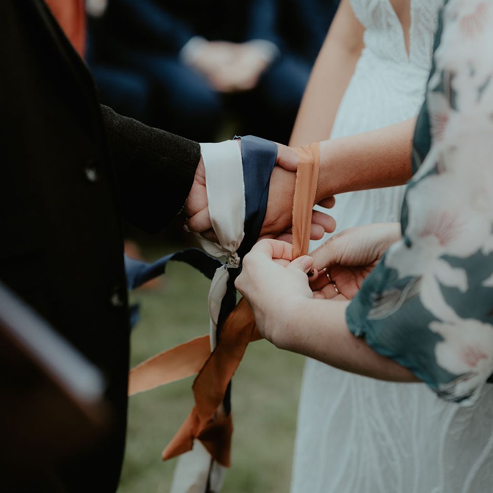 The bride and groom's hands are tied together with three different coloured ribbons for the handfasting ceremony 