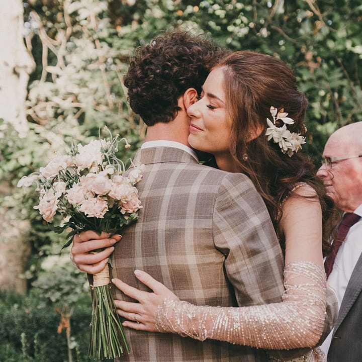 outdoor wedding ceremony in Spain with bride in a sparkly wedding dress embracing her husband in a check suit 