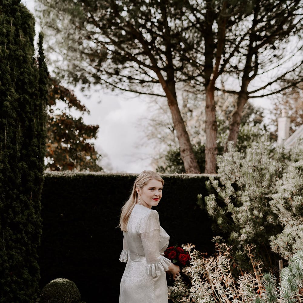 Bride with ruffle sleeves on silver metallic wedding dress with shoulder pads holding a red rose wedding bouquet 