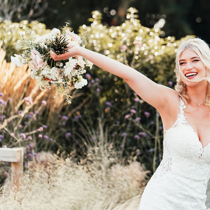 The bride in a lace wedding dress with thin straps and mermaid style skirt waving her wedding bouquet 