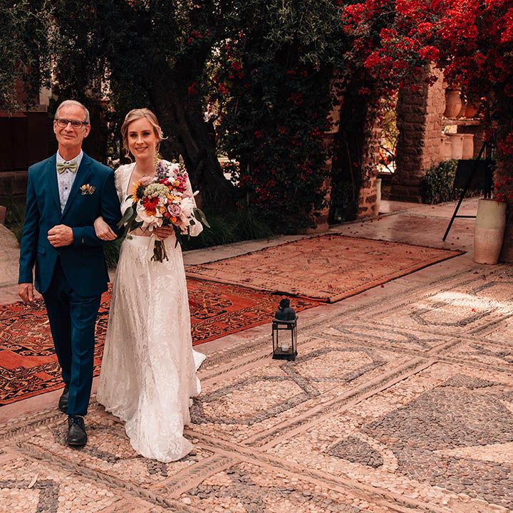 Groom in dark blue suit and light blue shirt with green bow tie walking arm in arm with the bride in modern lace separates 