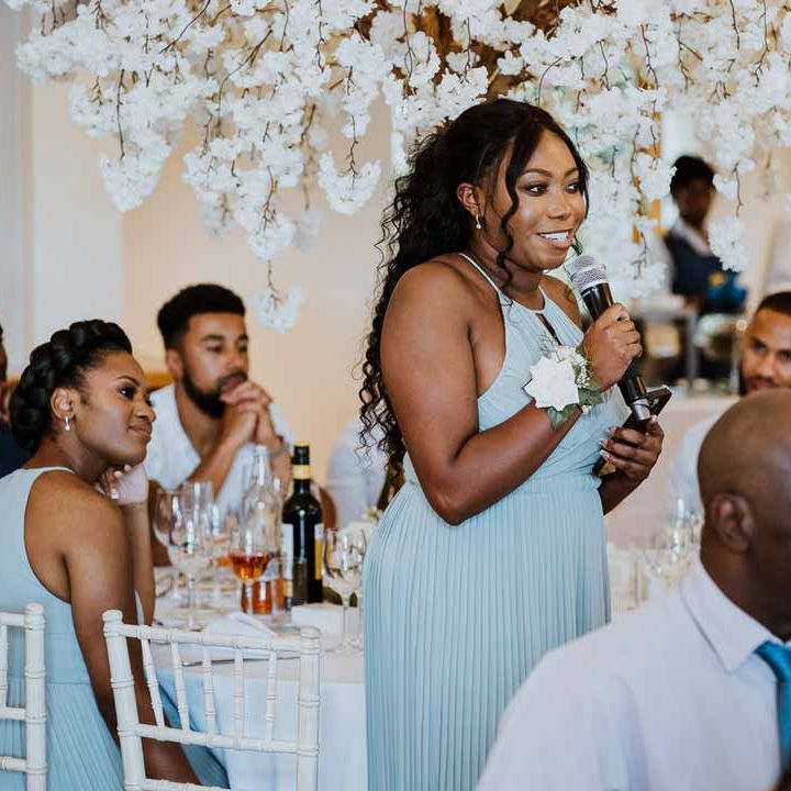 Bride in baby blue bridesmaid dress and white rose and foliage corsage doing emotional wedding speech 