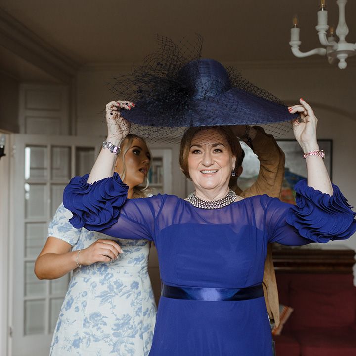 Mother of the bride puts on her dark blue hat wearing a dark blue dress for the wedding 