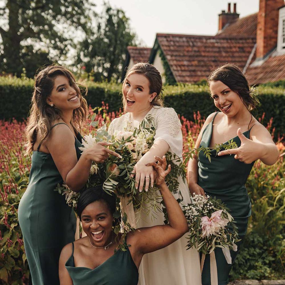 Bridesmaids in forest green slip bridesmaid dresses standing with bride in long sleeve lace wedding dress 