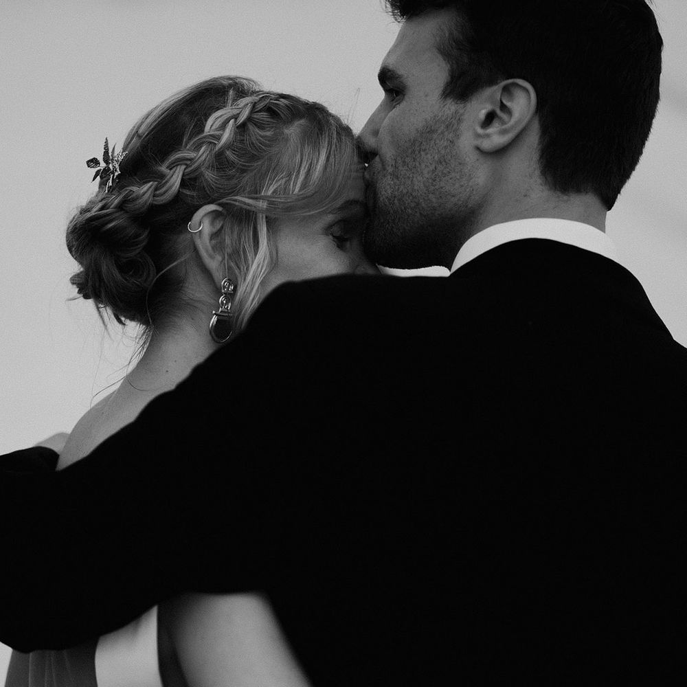 The groom romantically kisses the bride on the forehead in wedding photos 