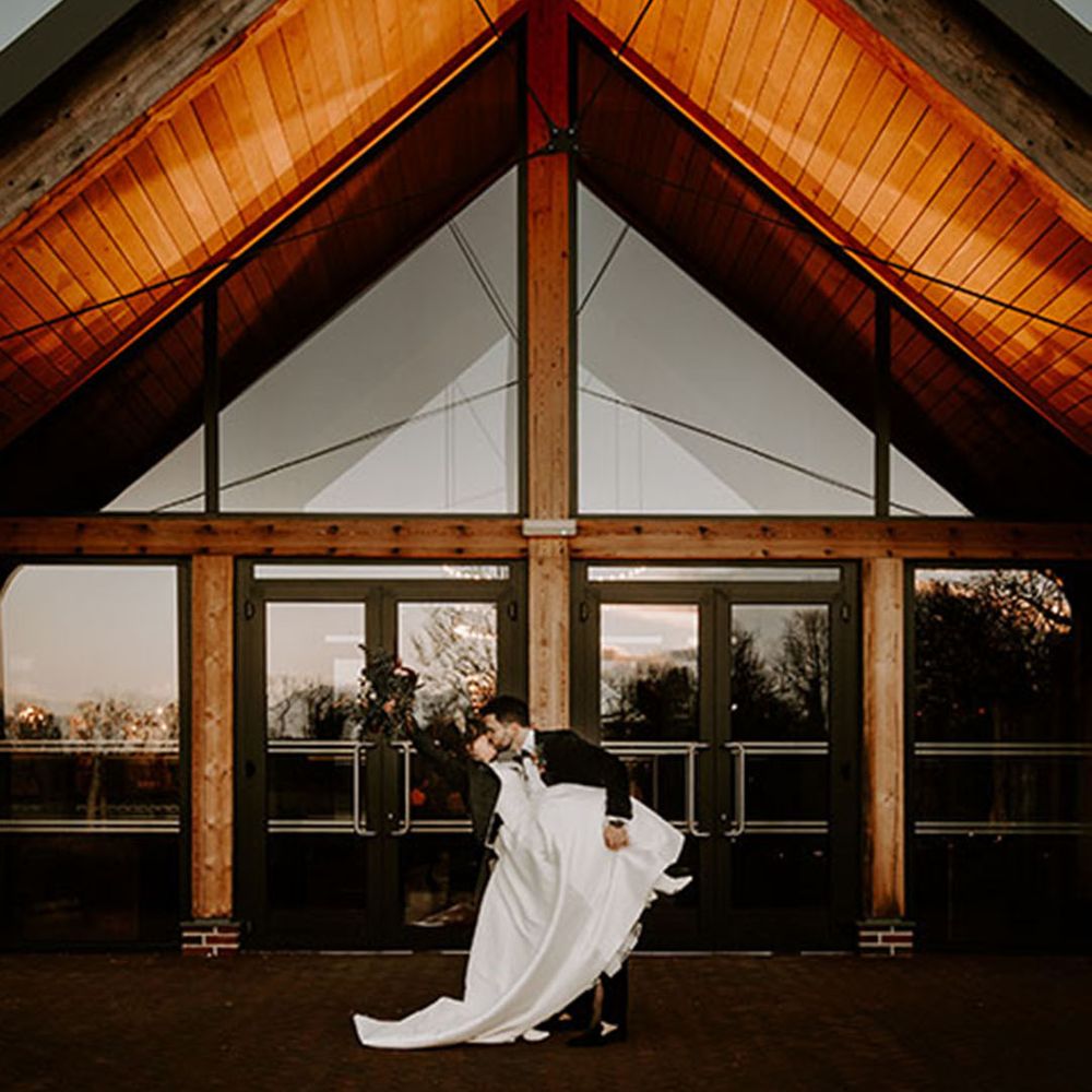 The bride and groom pose in front of the winter wedding venue 